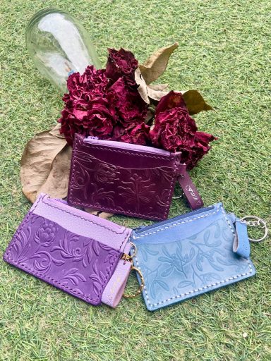 Three embossed cardholders in purple and blue, on a background of dried flowers.
